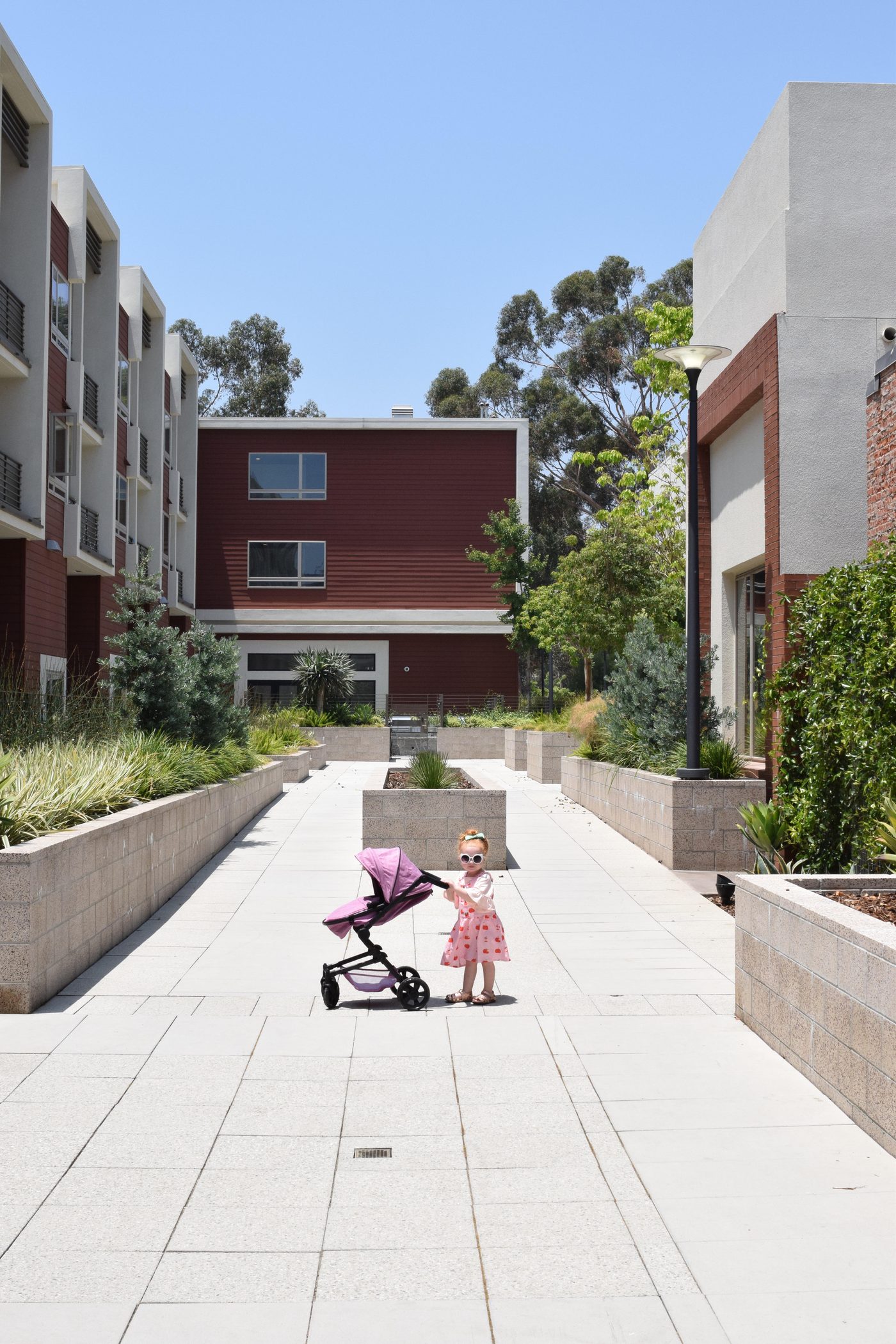 A small girl with her purple pram in a sunlit courtyard