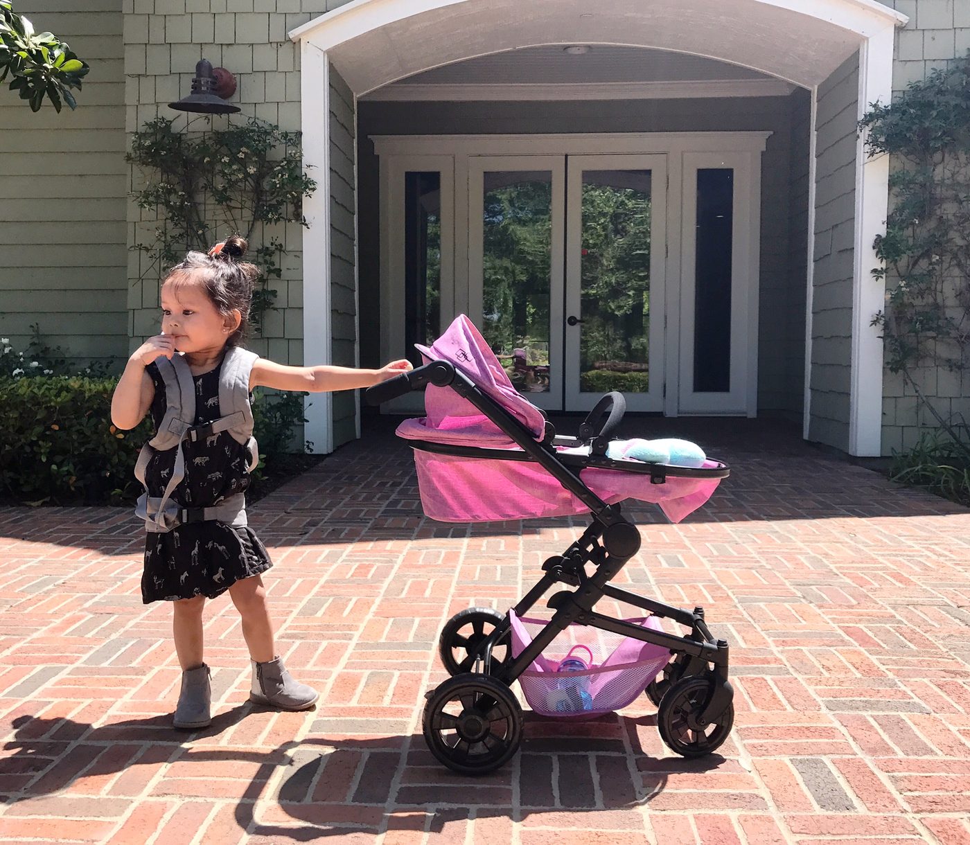 A toddler walking her pink pram across a brick courtyard